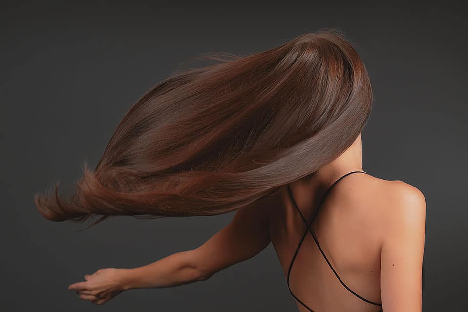 Brunette showing off long shiny hair waving on the wind. Hair care products and beautiful hair display. Woman standing back to camera.